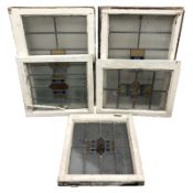 Five early 20th century stained and leaded glass windows in painted surrounds,