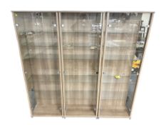 Three contemporary illuminated double door display cabinets, with glass shelves and keys,