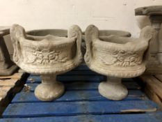A pair of concrete twin handled urns on stands,