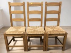 A set of three contemporary oak and rattan ladder back dining chairs.