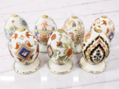 Seven Royal Crown Derby Eggs of the World porcelain eggs on stands, comprising Russia, Italy, India,