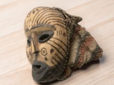 An African carved wooden ceremonial mask with wicker hood, height 24 cm.