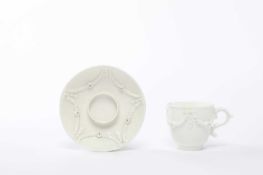 A MENNECY WHITE-GLAZED TREMBLEUSE CUP AND SAUCER C.1740 applied with relief, swags of leaves and