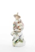 A MEISSEN FIGURE OF HARLEQUIN AFTER J J KÄNDLER, 18TH CENTURY seated on a rocky outcrop and