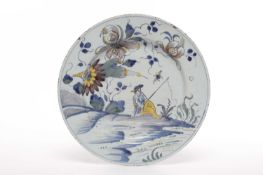 A DELFTWARE CHARGER LIVERPOOL, C.1750 polychrome painted with a fisherman before a flowering shrub