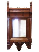 A Victorian gothic wall mirror in oak and walnut wood, supporting a shaped shelf and carved floral