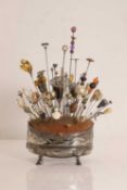 A collection of hatpins in a silver-plated pin cushion stand,