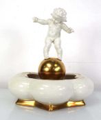 A Hutschenreuther table centre modelled as a putti standing on a gilt ball, h. 24.5 cm Some marks to