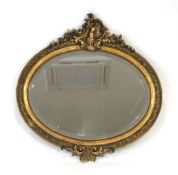 A late 19th century wall mirror, the bevelled oval plate within a gilt plaster frame surmounted by a