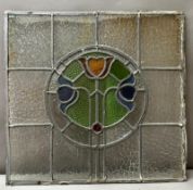 A stained glass panel in the Art Nouveau style featuring a central floral sheild in blue, green