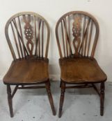 A pair of Windsor style dining chairs with wheel back splat and saddle seat