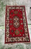 A wool prayer mat with red grounds, geometric border and central shield 143cm x 77cm