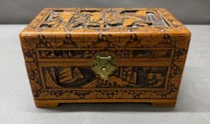 A heavily carved camphor wood trinket box featuring oriental scenes and brass fixings