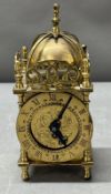 A brass lantern clock with turned finials and bell mounted top