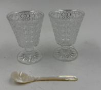 A pair of vintage glass spoon holders with a mother of pearl caviar spoon.