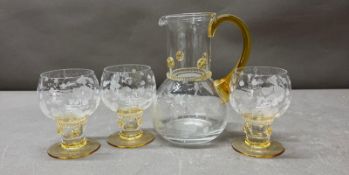 A yellow amber and clear glass pitcher and four matching glasses with an etched vine leaf motif