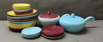 A selection of plates in yellow, blue and reds together with two lidded serving bowls