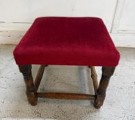 An oak footstool upholstered in red