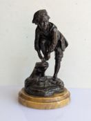 A caste and patinated bronze sculpture of a young man tying an ice skate to his shoe on a naturalist