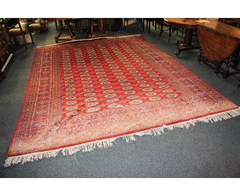 A wool Bokhara carpet, with six rows of elephant foot motifs and multi guard border on crimson ground, (af- one end faded, mo