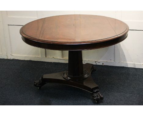 A Victorian mahogany circular tilt-top table on faceted pedestal triform base with carved lion's paw feet and castors, 113cm