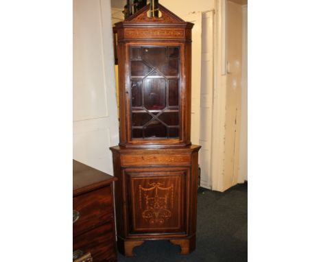 An Edwardian inlaid mahogany corner cupboard with panel glazed top, broken arch surmount above a panelled cupboard decorated 