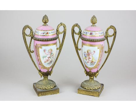 A pair of French gilt metal and porcelain vase shaped ornaments with twin scroll handles and flame finial, decorated with pan