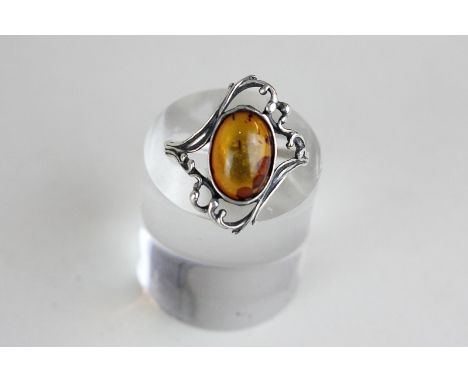 A silver ring with amber cabochon with scroll surround