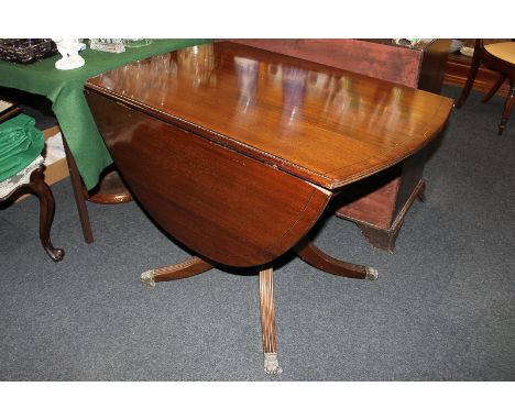 A Regency style mahogany drop-leaf oval table with ebony line inlay, on baluster pedestal and four fluted legs with brass paw