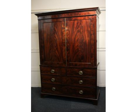 An early 19th century mahogany linen press with flame veneer panel doors enclosing shelves, above two short and two long draw