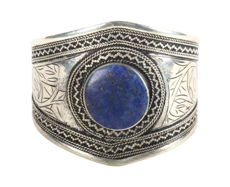 An unmarked Indian white metal torque bangle, with engraved decoration, set with a large circular lapis panel 