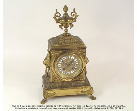 MANTEL CLOCK.A 19th century French brass mantel clock, with lion mask handles, urn finial & enamelled inset numerals. Movemen