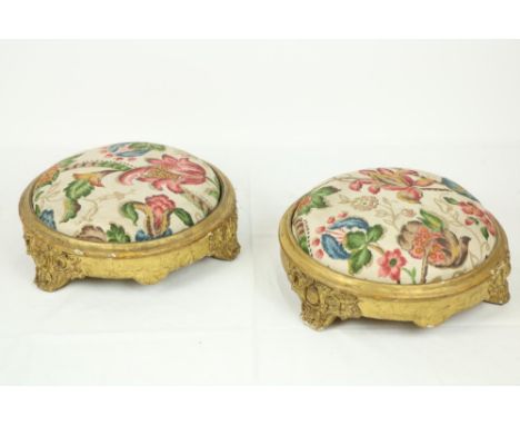 A pair of 19th Century circular gilt Footstools, each with scrolling foliage on three scroll legs, 12" (30cms), covered in ta
