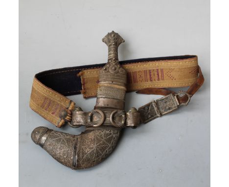 AN ARABIC 'JAMBIYA' TYPE DAGGER, with white metal covered grip, scabbard and belt fittings, on a woven fabric belt Buyers - f