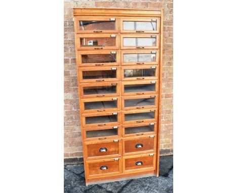 AN EARLY TWENTIETH CENTURY LIGHT OAK HABERDASHERS CABINET  fitted with sixteen glass fronted drawers above four further drawe