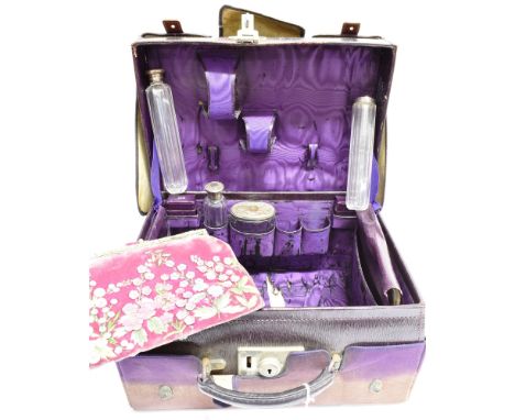 AN EARLY 20TH CENTURY MAROON LEATHER TRAVELLING TOILET CASE enclosing four white metal or silver mounted clear-glass toiletry