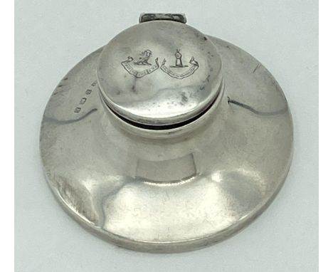 A silver hinge lidded capstan inkwell with clear glass liner and bakelite base. Lid is engraved with the crests of Clans Home