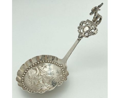 An antique Dutch silver tea caddy spoon with hooked handle. Bowl has scalloped rim and a decorative repousse featuring a Dutc