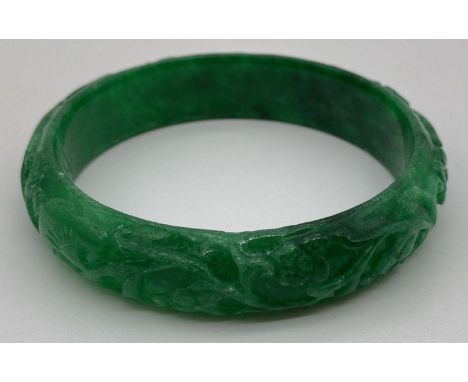 A green jade bangle with carved detail to outer surface. Approx. 7.5cm diameter.  