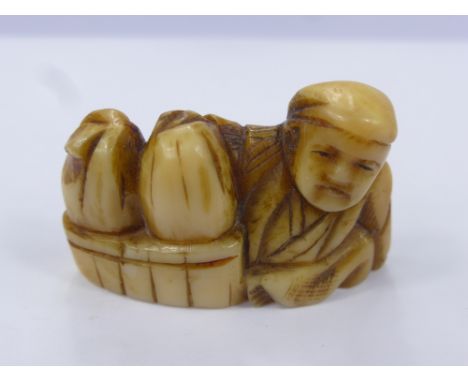 A Japanese Meiji Period Ivory Netsuke, the figure carved in the form of a merchant with baskets at his side.