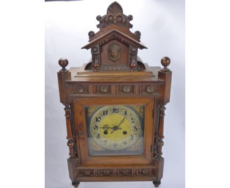 An Edwardian Continental Oak Case Mantle Clock, the clock having silvered and gold face and chapter dial with carved wooden m