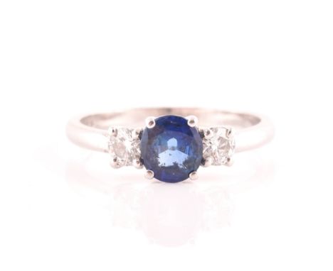 An 18ct white gold, diamond, and sapphire ring, set with a mixed round-cut blue sapphire, flanked with two round brilliant-cu