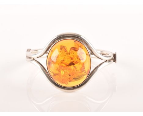 A silver and amber bangle bracelet, set with a large oval cabochon amber, measuring approximately 3.7 x 3.3 cm, in open shoul