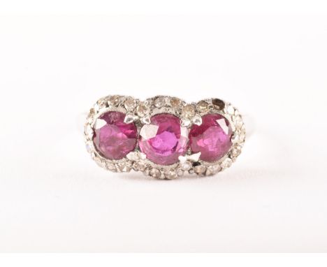 A early 20th century white metal cluster ring, featuring three round old cut rubies with a combined approximate weight of 2.2