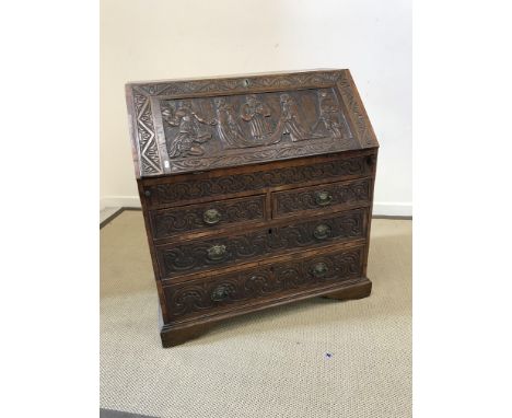 An 18th Century oak bureau with later carved decoration in the Gothic Revival taste, the plain top over a sloping fall decora