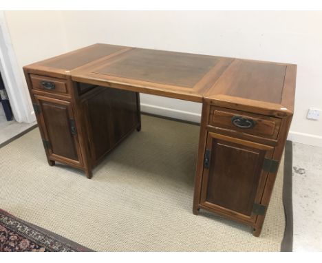 A 20th Century Chinese walnut desk, the central panel flanked by two pedestals with drawers over cupboard doors, on scroll fe