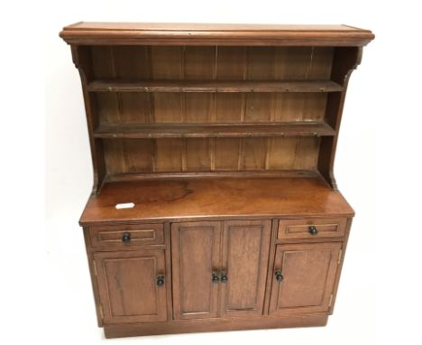 An Arts &amp; Crafts miniature walnut dresser by D Rolyat of Battersea, the boarded two tier plate rack with brass cup hooks 