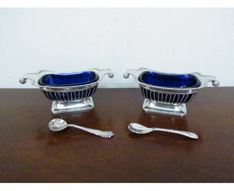 A pair of Millar & Wilkinson silver salts of boat form with scroll ends, blue glass liners and associated spoons, London 1910