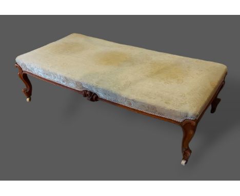 A large Victorian walnut footstool, the upholstered seat above a carved frieze raised upon carved cabriole legs, 133cms x 66c