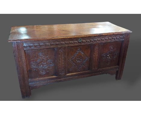 An 18th Century oak Coffer, the hinged top above a triple carved panel front flanked by stiles, 141cms wide, 58cms deep and 7